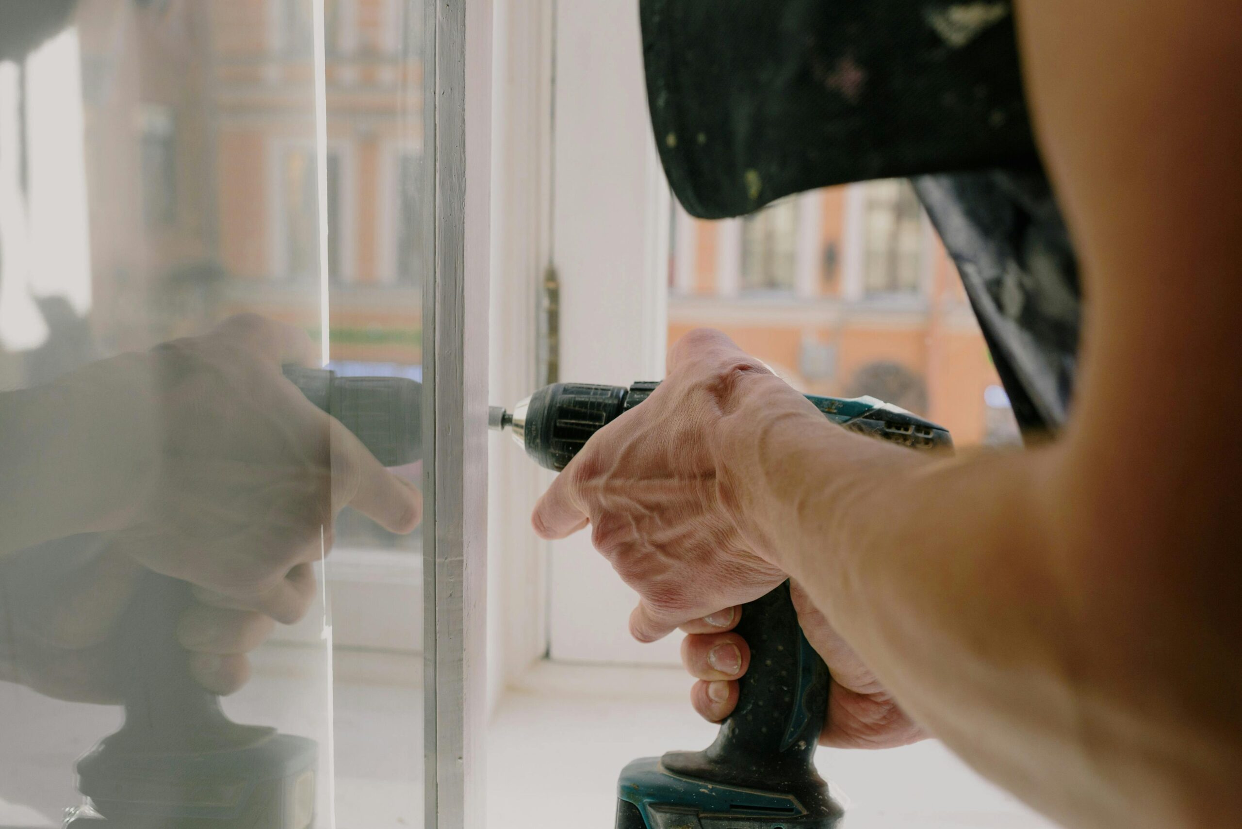 Close-up of a handyman's hands using a drill to fix a window inside an apartment.